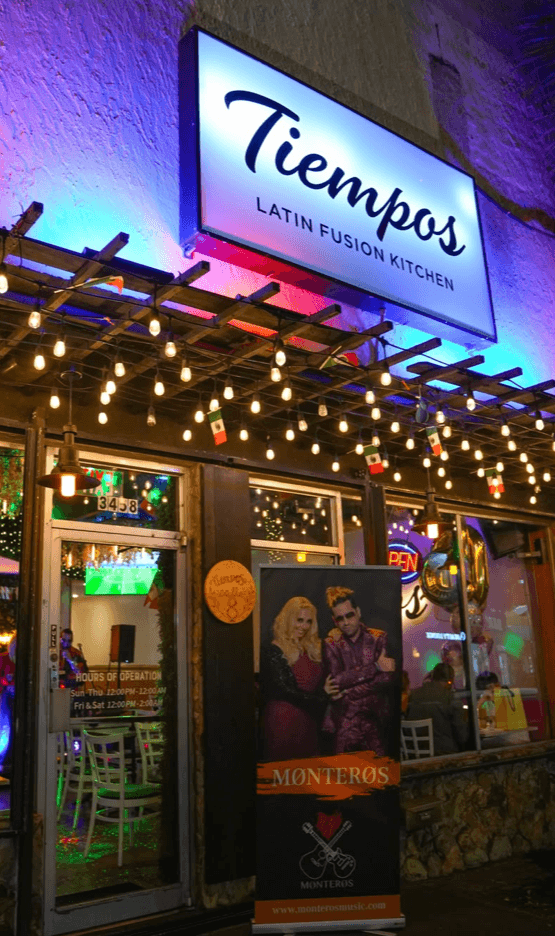 Tiempo D' Tacos entrance on SW 8th Street at night with string lights, Mexican flags, and the Monteros live music banner